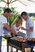 One woman and two men barbecuing food