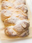 Bread plait with flaked almonds & icing sugar on baking parchment
