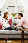 Man and pregnant woman drinking tea on sofa