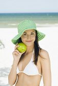 Young woman in sun hat with green apple on beach