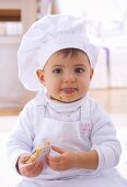 Kleines Mädchen mit Kochmütze isst Plätzchen