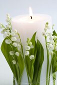 Burning white candle with lilies of the valley