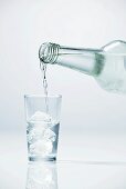 Pouring vodka into glass containing ice cubes