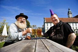 Man with Mohawk hairstyle & man in Bavarian dress in beer garden
