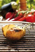 Barbecued potato on barbecue, vegetables in background