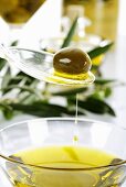 Olive und Olivenöl auf Plastiklöffel über Glasschale mit Olivenöl