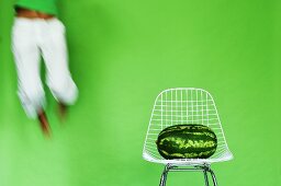 Young woman jumping by watermelon on chair, (blurred motion)