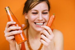 Young woman holding carrot and carrot juice, smiling, close-up