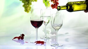 Pouring white wine into glass, glass of red wine, grapes, autumn leaves