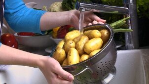 Kartoffeln in einem Sieb unter fliessendem Wasser waschen