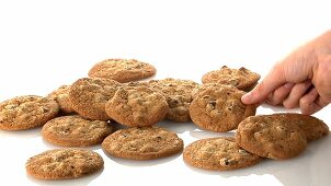 A pile of chocolate chip cookies and a hand taking one