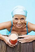 Germany, senior woman having cocktail at pool