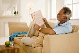 Mature man reading newspaper on sofa, side view