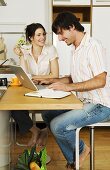 Young couple in kitchen, man using laptop, smiling