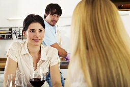 Three young people drinking wine in kitchen, close-up