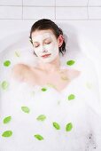 Young woman with face mask taking a bubble bath, eyes closed