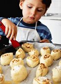 Little boy brushing cinnamon buns with butter