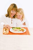 Mother & daughter sitting at table in front of vegetable terrine