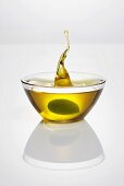 Grüne Olive fällt in Glasschale mit Olivenöl