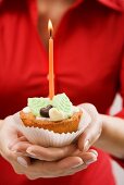 Woman holding cupcake with marzipan leaves and candle