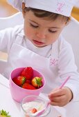 Kleines Mädchen mit Kochmütze isst Erdbeeren