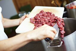 Koch kippt geschnittenes Rindfleisch in Kochtopf