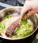 Sprinkling fried pork fillet in frying pan with cress