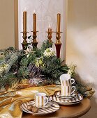 Adventsgesteck und getreifte Tassen auf einem goldenen Tisch