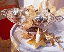 Silver bowl with baubles, stars and ribbon besides lit candle