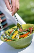 Close-up of woman's hands mixing Italian bean salad with spoon in green bowl