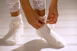 Close-up of woman tying the bow of white woolen socks on her feet