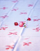 Rosa-rote Blueten liegen auf einem weissen Tuch mit Blumendruck,Nr.3
