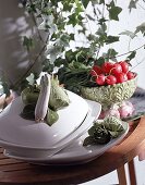 Weißes Keramikgeschirr mit handbemalten Gemüsereliefs.