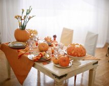 Gedeckter Tisch mit Kürbissen dekoriert, orange Farben.