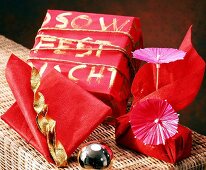Geschenke, verpackt mit rotem Vliespapier, Goldschnur u. Papierschirmen