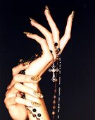 Close-up of woman's hand wearing colourful nail polish holding rosary