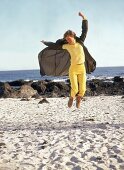Frau trägt dunkelbraunen ParkaMantel+gelbe Hose+Shirt,springt