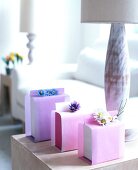 Three gifts wrapped with fabric flowers and pink tissue paper on table