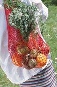 rotes Einkaufsnetz mit Orangen,Möhre Äpfeln, Avocado von Frau getragen