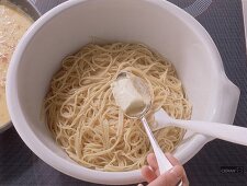 Butter wird in einer Schüssel mit den Spaghetti verrührt