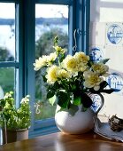 Henkeltopf mit weißen Dahlien vor blauem Sprossenfenster