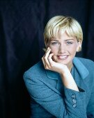 Portrait of blonde woman with bob and bangs in blue suit with hand on chin, smiling