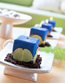 Four blue lit candles on silver tray decorated with sheet, leaves and gold wire