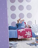 Frau liegt auf Bett, weiße Tapete mit großen lila Kreisen