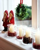 White pillar candles in jars covered with star anise and pink pepper on window sill