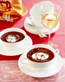 Red beet soup with horseradish garnished with cream on table with glass of white wine