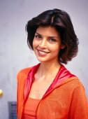 Portrait of young woman with dark hair wearing orange-red hooded jacket, smiling