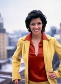 Portrait of young woman with dark hair wearing yellow blazer over red blouse, smiling