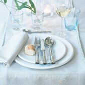Close-up of silverware on white crockery and glasses on organza table runner