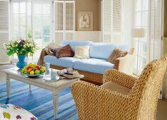 Wicker sofa and armchair with blue cushions and table with flower vase in living room